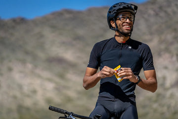 Athlete resting on bicycle and opening packet of SaltStick Tropical Mango chewable electrolytes