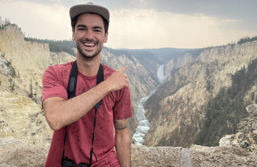 Noah posing with binoculars above a canyon with a flowing river.