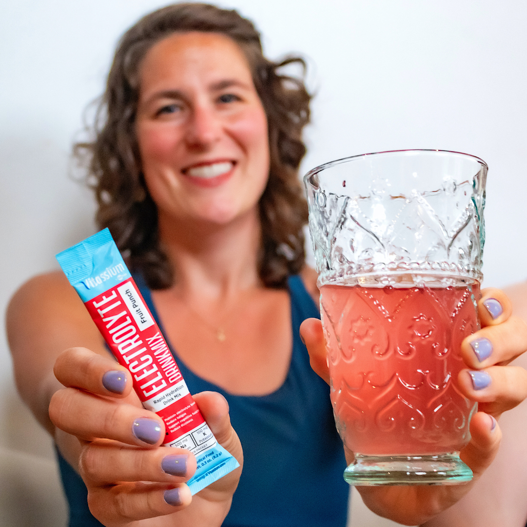 Woman holding Vitassium DrinkMix stick pack and glass of DrinkMix