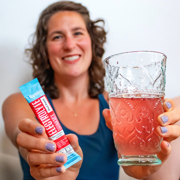 Woman holding Vitassium DrinkMix stick pack and glass of DrinkMix
