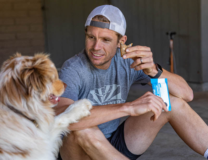 Jason Winn eating a Bonk Breaker bar with his dog by his side