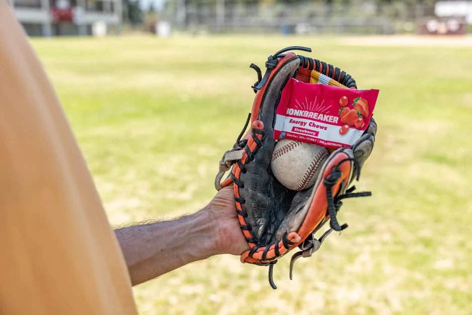 A man's hand in a baseball glove holding a ball and Bonk Breaker Energy Chews.