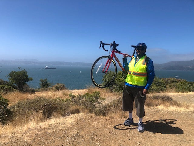 Vellay holding his bike up with a view of the San Francisco Bay behind.