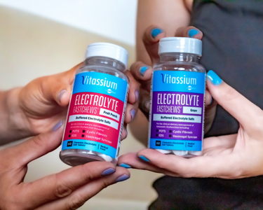 Two pairs of hands hold a bottle of Vitassium Fruit Punch FastChews and a bottle of Vitassium Grape FastChews.