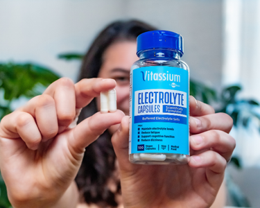 A person holds a bottle of Vitassium Capsules in one hand and two capsules in the other hand. 