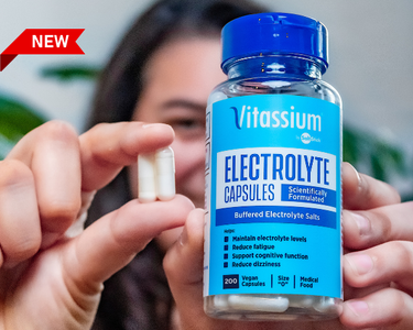 A Vitassium fan holds up a 200ct bottle of Vitassium Capsules in one hand, and two Capsules in the other hand.