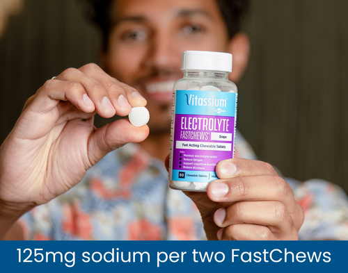 Man holding a bottle of Vitassium Grape Electrolyte FastChews and one white chewable tablet, labeled 125 mg sodium per two FastChews.