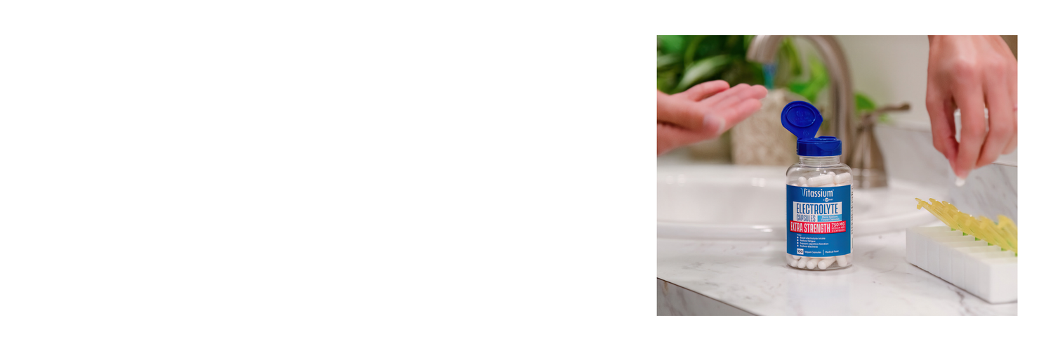Vitassium Electrolyte Capsules Extra Strength with 750 mg sodium, open bottle on a bathroom counter as a person pours capsules into their hand.