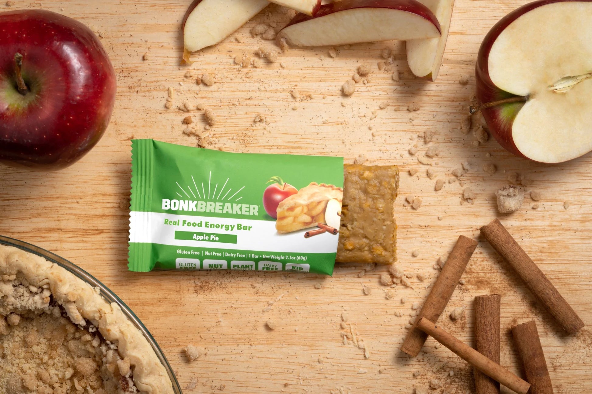 Bonk Breaker Apple Pie Real Food Energy Bar on a table with apples, cinnamon, and apple pie