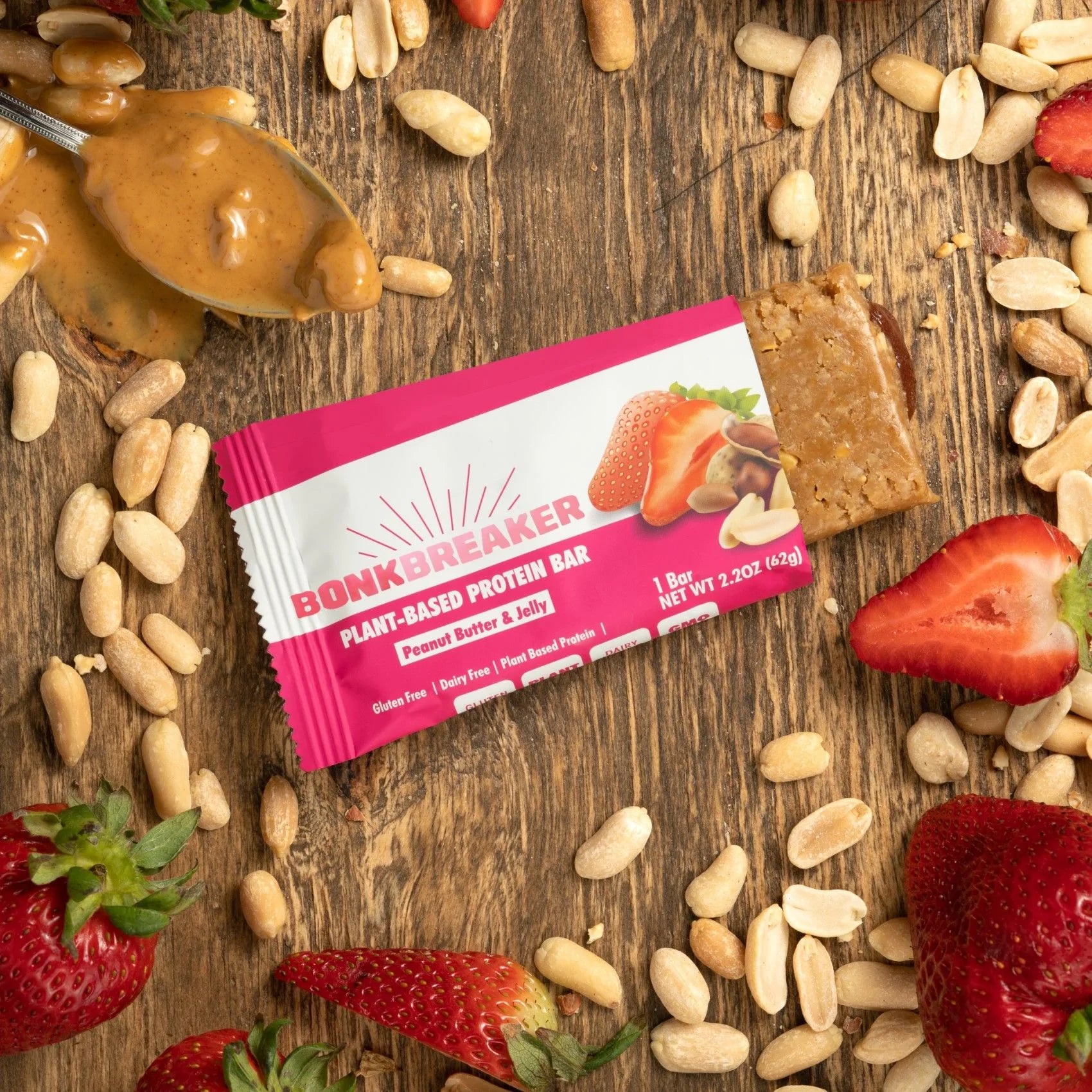 Bonk Breaker Peanut Butter and Jelly Plant-Based Protein Bar on a table with peanuts, peanut butter, and strawberries